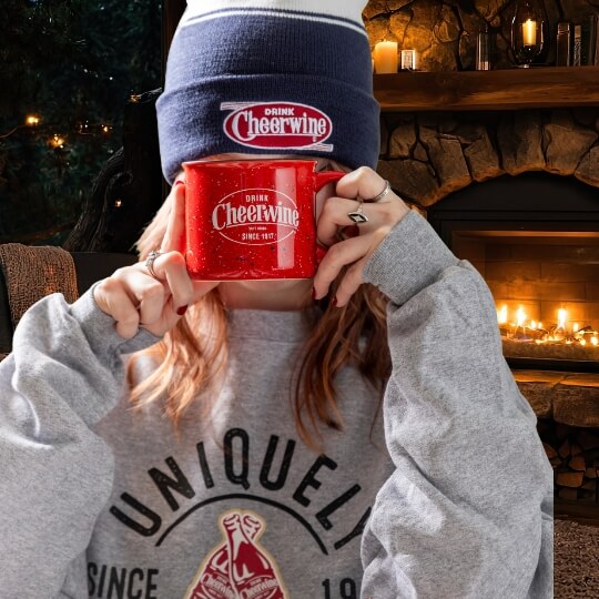 woman wearing Cheerwine merchandise holding up a Cheerwine coffee mug