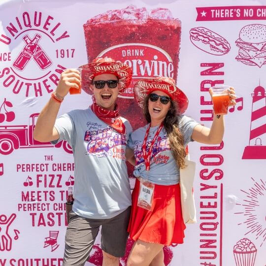 Two people posing at the Cheerwine festival holding up Cheerwine